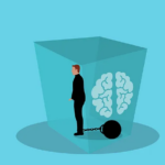 A man inside a cube. He is held back by a ball and chain. There is an image of a brain in the box with the man.